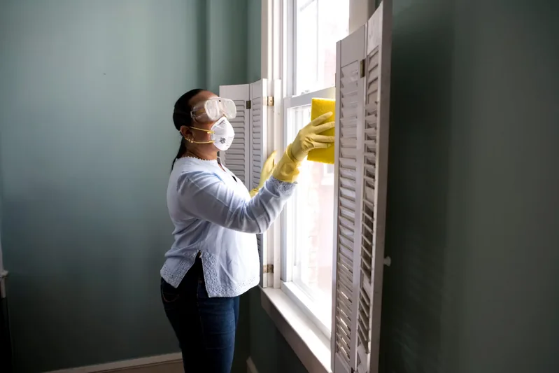 Careful cleaning of white timber shutters in a home.